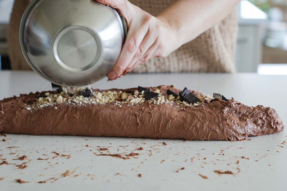 Chocolate chunks and crushed almonds sprinkles at top of log dough.