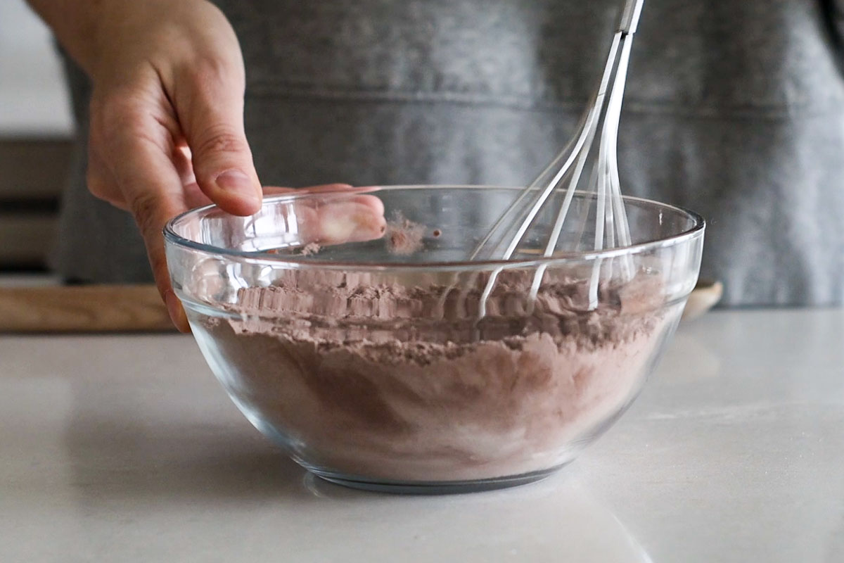 Hand whisking dry ingredients in a glass bowl.