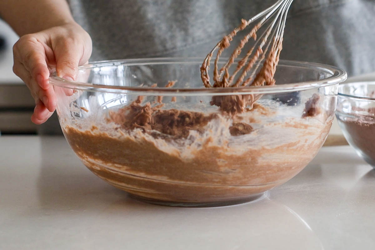 Hand whisking wet ingredients in a glass bowl.