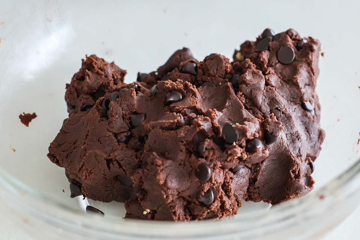 Chocolate cookie dough with chocolate chips inside glass bowl.