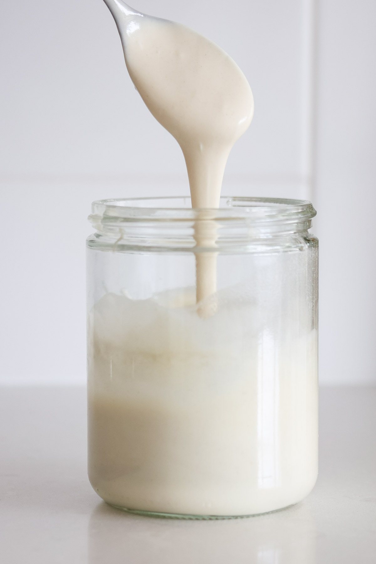 Thin sourdough starter pouring of a spoon into a jar.