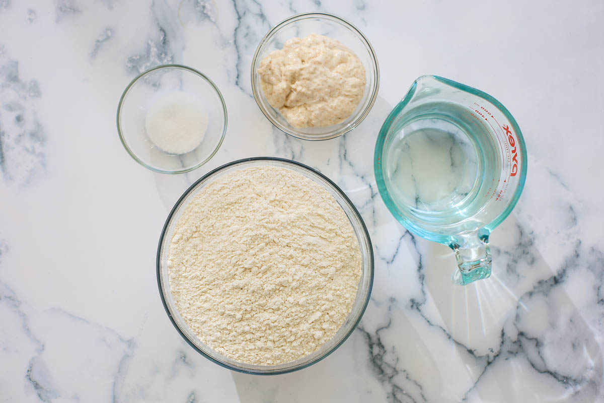 Recipe ingredientes into glass containers: flour, water, salt and sourdough starter.