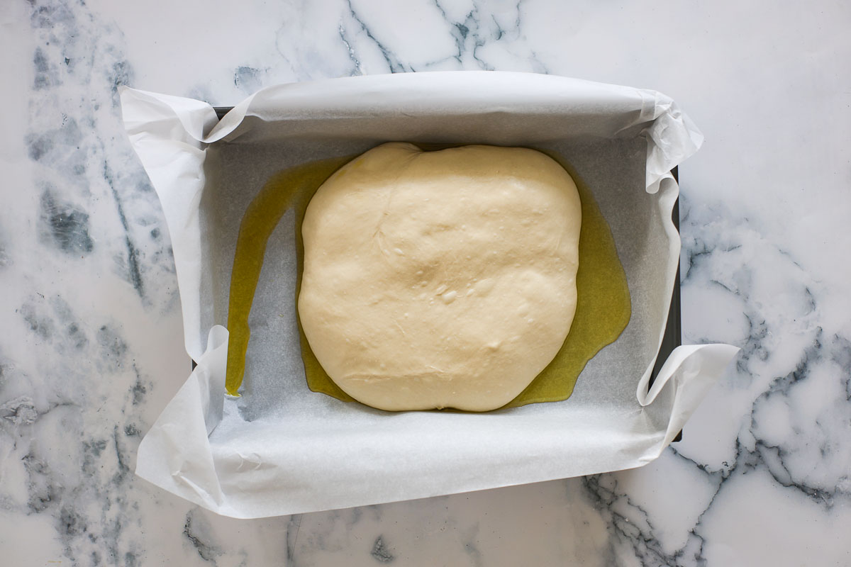 Dough inside a baking pan on top of parchment papel and olive oil.