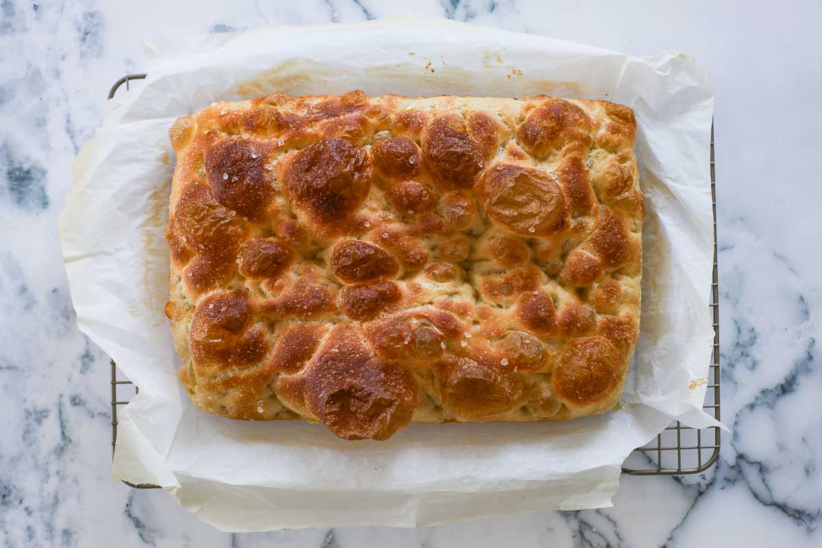 Baked focaccia on top of parchment paper and cooling rack.