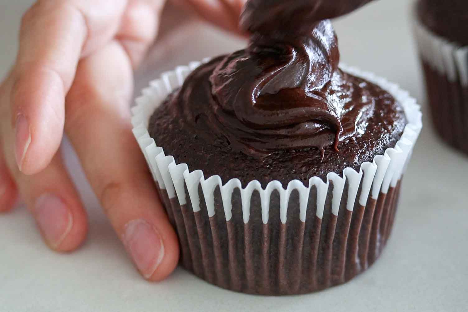 A spoon that spreads chocolate ganache on a cupcake.